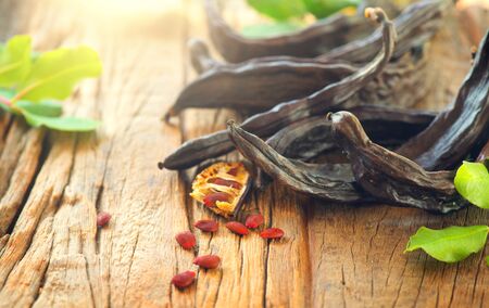 Carob. Healthy organic sweet carob pods with seeds and leaves on a wooden table.の写真素材