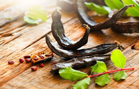 Carob. Healthy organic sweet carob pods with seeds and leaves on a wooden table.の写真素材