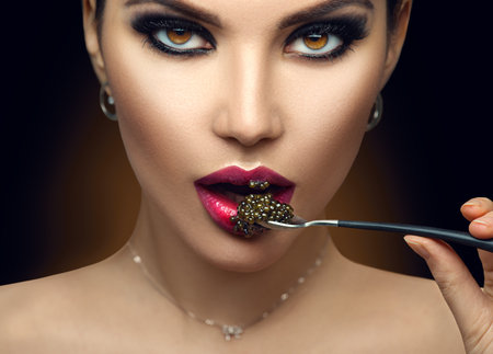 Beautiful Fashion Model woman eating black caviar.