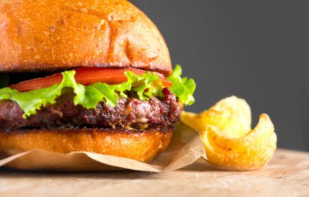 Hamburger with fries rotated on wooden table background. Cheeseburgers on fresh buns with succulent beef and fresh salad ingredients served with French Fries. Close upの写真素材