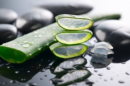 Aloe Vera slices and spa stones closeup. Aloevera plant leaf gel, natural organic renewal cosmetics, alternative medicine. Skin care concept. Skincare. Moisturizing. On black backgroundの写真素材