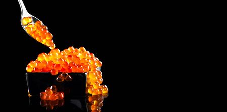 Red Caviar in a spoon. Caviar in bowl over black background. Close-up salmon caviar. Delicatessen. Gourmet food. Texture of caviar. Seafood isolated on blackの写真素材