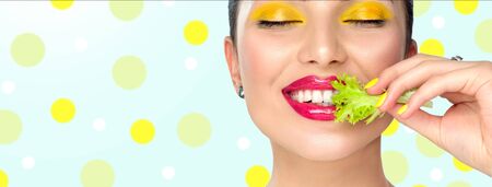 Healthy eating, diet. Beautiful healthy girl eating raw vegan food and smiling. Beauty young fashion woman eats green fresh lettuce salad leaf, organic vegetables. Vegetarian concept. Makeup.の写真素材