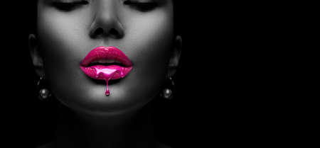 Purple Paint dripping, lipgloss drops on sexy lips, bright liquid paint on beautiful model girl's mouth, black skin. Lipstick. Make-up. Beauty face makeup, close up. Isolated on black backgroundの写真素材