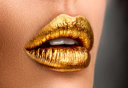 Golden lipstick closeup. Metal gold lips. Beautiful makeup. Sexy lips, bright paint on beautiful model girl's mouth, close-up. Metallic Lipstick closeup. Isolated on black backgroundの写真素材