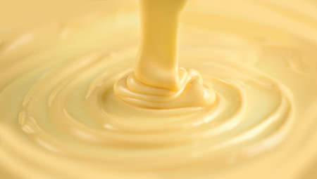 White Chocolate. Pouring melted liquid premium milk white chocolate. Close up of molten liquid hot chocolate swirl. Confectionery. Confectioner prepares dessert, icing.の写真素材