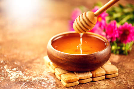 Honey dripping from honey dipper in wooden bowl.  Close-up. Healthy organic thick honey dipping from the wooden honey spoon, closeupの写真素材