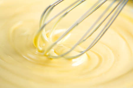 White Chocolate mixing with a whisk. Pouring melted liquid premium milk white chocolate. Close up of molten liquid hot chocolate swirl. Confectionery. Confectioner prepares dessert, icingの写真素材