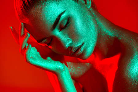 High Fashion model woman in colorful bright sparkles and neon lights posing in studio, portrait of beautiful sexy girl, trendy glowing sequins make-up. Art design make up. Glitter Vivid makeupの写真素材