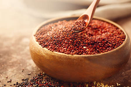 Red quinoa grains in a wooden spoon. Healthy food in a bowl. Seeds of red quinoa - Chenopodium quinoa. Healthy vegan foodの写真素材