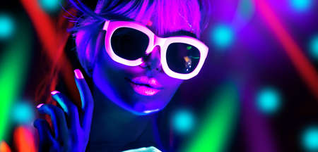 Disco dancer in neon light in night club Fashion model woman in neon light, portrait of beautiful girl with fluorescent make-up, Body Art design in UV, sunglasses, colorful make up.の写真素材