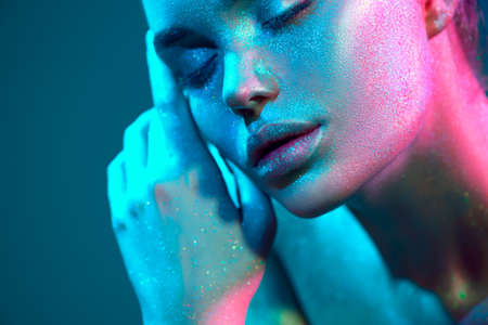 Fashion art. Model girl in colorful bright sparkles and neon lights posing in studio, portrait of beautiful woman, trendy glowing sequins make-up. Design. Make up. Glitter Vivid makeup.の写真素材