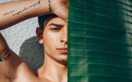 Young man fashion art portrait. Handsome male close up. Portrait of sexy muscular guy, looking at camera. Fashion urban boy posing with banana leafの写真素材