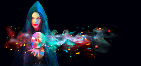 Halloween Witch woman holding human skull lantern in her hands. Beautiful young girl. Darkness. Scary backdrop. Over black background. Magic concept. Art designの写真素材