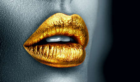 Golden lipstick closeup. Metal gold lips. Beautiful makeup. Sexy lips, bright paint on beautiful model girl's mouth, close-up. Clack and white. Metallic Lipstick closeup. Isolated on black backgroundの写真素材