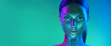 Glowing metallic skin. Fashion model woman face in bright neon colourful lights, beautiful sexy woman, UV, ultraviolet trendy make-up. Art design make up. Glittering, golden, metallic shine makeupの写真素材