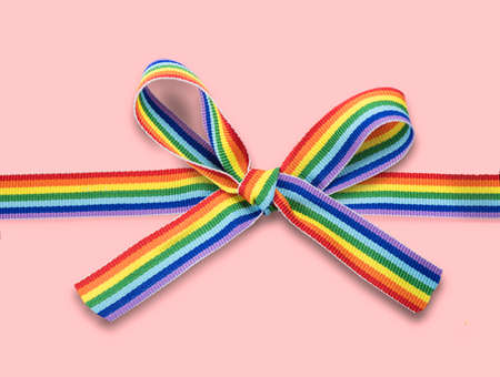 Colorful rainbow ribbon bow. LGBT colourful design, isolated on pink background. Gay pride design. Ribbon or banner with flag of LGBTQ pride border. Gift.の写真素材