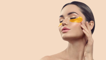 Woman with under eye collagen gold pads, patches, beauty model girl face with healthy skin. Skin care concept, anti-aging moisturizing eye mask, golden hydrogel, eye skin treatmentの写真素材