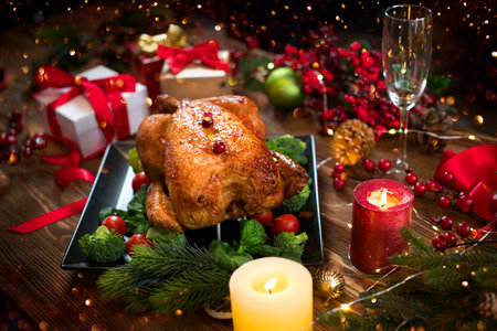 Christmas Dinner. Roasted chicken. Winter Holiday table served, decorated with candles and xmas baubles. Roast turkey over wooden background with Christmas tree, table setting famiの写真素材
