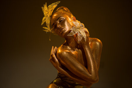 High Fashion gold model woman with bright golden sparkles on skin, fantasy flower, portrait of beautiful girl glowing make-up. Art design gold dust sequins make up. Glitter glowingの写真素材
