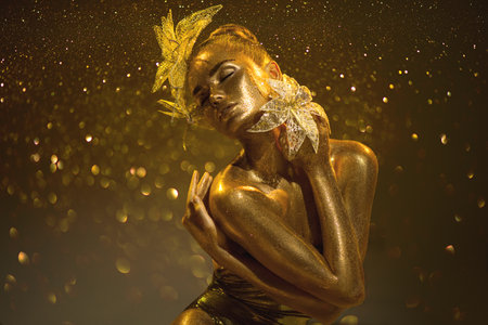 High Fashion gold model woman with bright golden sparkles on skin, fantasy flower, portrait of beautiful girl glowing make-up. Art design gold dust sequins make up. Glitter glowingの写真素材