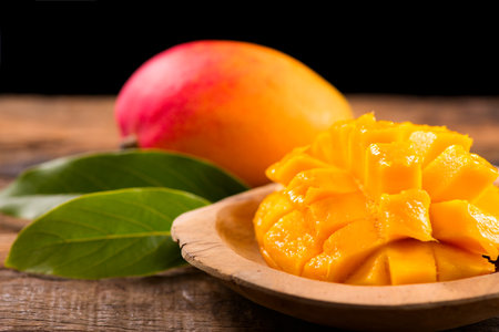 Mango fruit. Ripe Mango fruits on wooden table over black background. Close-up of fresh juicy tropical mango with leaf, ready to eat healthy sweet dessert, vegan food.の写真素材