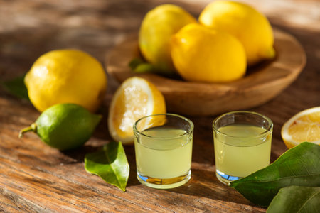 Limoncello, Italian liqueur with lemons. Traditional Mediterranean sweet shot alcoholic drink close up, little glasses and fresh citrus fruits on wooden tableの写真素材