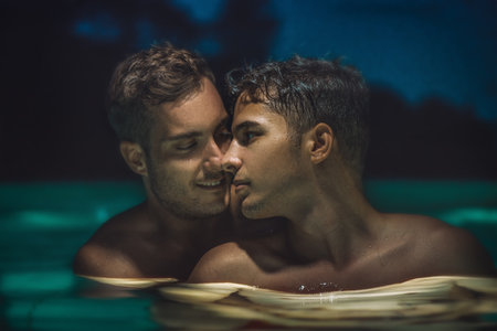 Gay couple relaxing in swimming pool at night. LGBT. Two young men kissing and hugging. Young men romantic family in love. Happiness conceptの写真素材