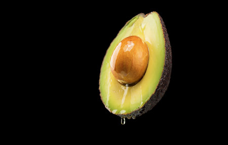 Avocado oil pouring, dripping essential oil on cut avocado isolated on black background. Fresh cut avocado with oil stream. Concept of healthy fruit for eating or cosmetics. Veganの写真素材