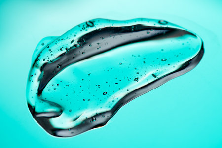 Transparent gel drop. Liquid cream gel cosmetic smudge texture on blue background. Cosmetics serum gel, hyaluronic acid cream background, facial treatment, fluid.の写真素材