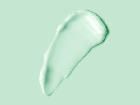 Green cream smear over light green background. Cosmetic hydration cream smudge of liquid reach face or body cream, balm mask texture, top view. Skin care, facial cream, lotion. Herの写真素材