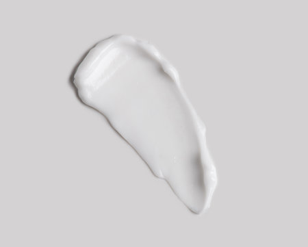 White cream smear over grey background. Cosmetic hydration cream smudge of liquid reach face or body cream, balm mask texture, top view. Skin care, facial cream, lotionの写真素材