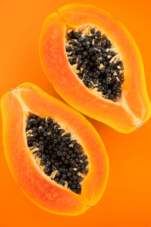 Papaya fruits on orange, yellow background. Halved fresh organic Papaya exotic fruit backdrop, top...
