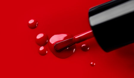 Red nail polish drops, manicure concept. Spilled uv gel, enamel, varnish with brush on red color background, splash. Beauty salon, nail care product. Nail art. Top view, fashion baの写真素材