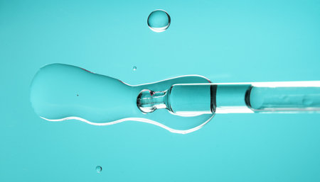 Cosmetic dropper with serum, beauty cosmetics dripping, on blue background. Macro shot. Serum, peptides, beauty and health care products. Glass pipette with liquid close up. Top viの写真素材