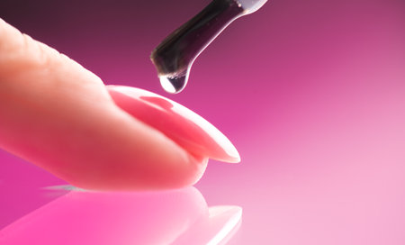 Applying Nail polish, pink shellac UV gel, varnish, manicure process concept in beauty salon. Transparent top coat drop on brush. Over pink background. Application of nail polishの写真素材