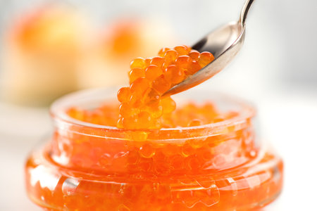Red Caviar in a spoon, fish roe in a glass jar. Close-up of salmon fish roe caviar on served table. Delicatessen. Texture of fresh trout caviar. Backdrop. Seafood.の写真素材