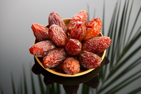 Dates fruit. Date fruits with palm tree leaf reflection on black background. Heap of Medjool dates in wooden bowl close up. Tasty healthy Foodの写真素材