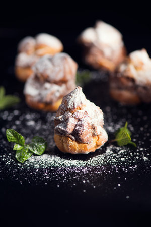 Profiteroles or cream puff with filling,  falling powder sugar topping. Berries, mint on black background. Fresh homemade Cream Puffs, cake, tasty French choux puff, ecler, dessertの写真素材
