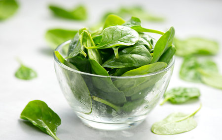Spinach in a transparent glass bowl on light gray table background. Heap of Baby spinach fresh...