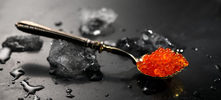 Red caviar in a spoon over black stone background, with ice. Red Caviar in a spoon art design....