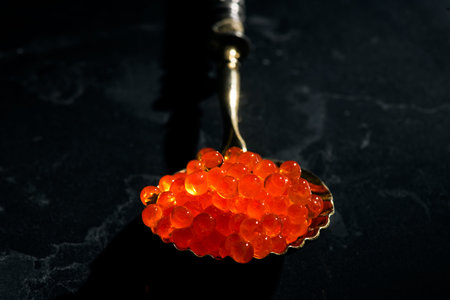 Red caviar in a spoon over black stone background, close up. Red Caviar in a spoon art design....