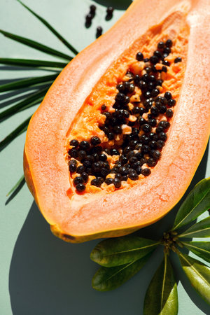 Papaya fruit over green background, fresh exotic fruits with leaves and seeds. Halved fresh organic Papaya exotic fruit art design, close up, vertical imageの写真素材