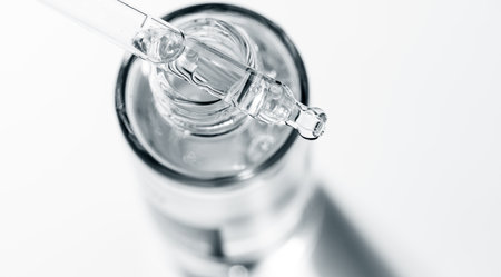 Cosmetic dropper with serum, essential oil, beauty cosmetics dripping, on grey background. Macro shot. Serum, peptides, beauty and health care products. Glass pipette with liquid.の写真素材