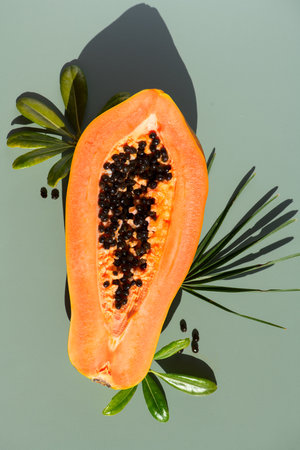 Papaya fruit over green background, fresh exotic fruits with leaves and seeds. Halved fresh organic Papaya exotic fruit art design, close up. Top view, vertical imageの写真素材