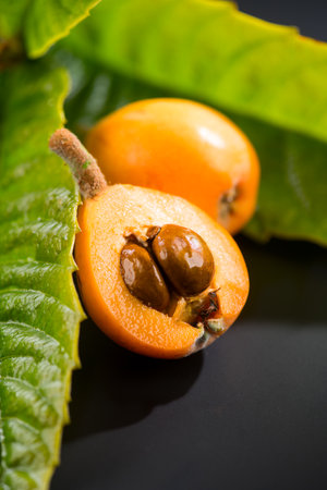 Loquat fruit or Japanese medlars, Nispero, Eriobotrya japonica with leaves fresh ripe bio vegetarian food, medlar berries. Close up. On black background table. Vertical imageの写真素材