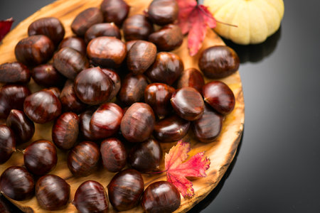 Chestnut, Fresh sweet chestnuts with autumn red leaves and little decorative pumpkin on black background, top view. Thanksgiving day. Edible chestnuts (Castanea sativa) in wooden bの写真素材