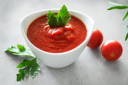Tomato sauce, Homemade tomato paste in a white bowl and fresh ingredients on a grey table. Ketchup, Red sauce for pizza or pasta made from fresh bio tomatoes.の写真素材