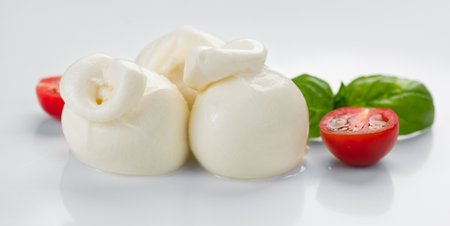 Burrata cheese, tasty Burrata soft cheese with basil leaves and tomatoes on white background, close up. Italian food.の写真素材