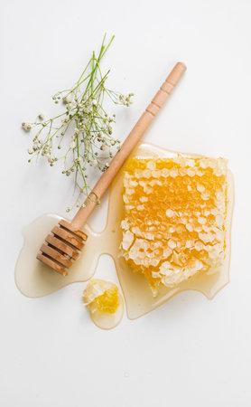Honey in honeycombs dripping, pouring from wooden honey dipper spoon, on white background. Close-up....
